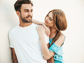 Portrait of smiling beautiful female and her handsome boyfriend. Woman in casual summer jeans dress. Happy cheerful family. Couple posing in the street near white wall