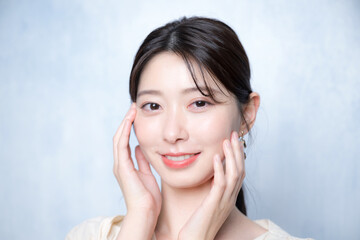 水色背景でお肌を気にする艶感や透明感のある若い女性のクローズアップのカメラ目線　ピンクメイクの美容やビューティーにも