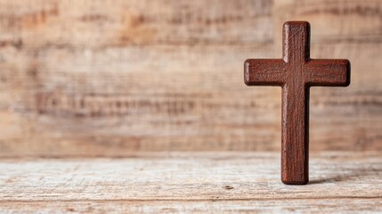 A simple dark brown wooden cross stands upright on a rustic light brown wooden surface against a blurred wooden background.