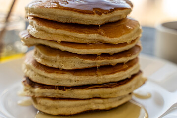 Pancakes poured with honey on a white plate with napkin and coffee on a gray background. Selected Focus
