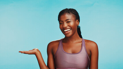 Black woman, fitness and portrait with mockup space, sports announcement and happy in studio. Personal trainer, smile or showing gesture on blue background for gym sign up promotion or membership