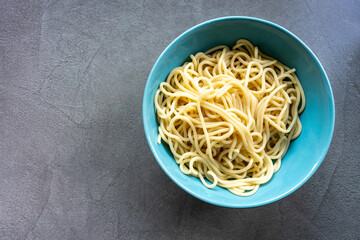 Cooked spaghetti in a blue bowl on gray background