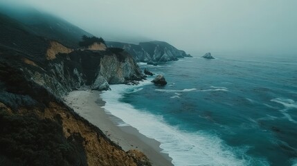 Coastal cliffs meet a beach under a foggy atmospheric sky