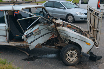 The aftermath of a traffic accident on a city road, close-up. A car with a broken front end and an open hood is at the scene of the accident. Broken windshield.