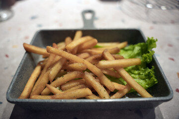 Golden French fries are served in a metal tray and placed on top of fresh green lettuce leaves when served.