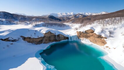 Frozen waterfall cascades into a vibrant turquoise pool nestled within a snow-covered mountain landscape