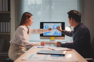 Two business colleagues are pointing at charts displayed on a computer screen, analyzing data and...