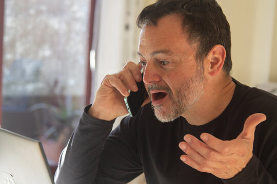 middle aged man working with pc while talking on phone at home or workplace.