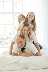 Obraz premium Happy parents and their daughter having fun on a bed indoors