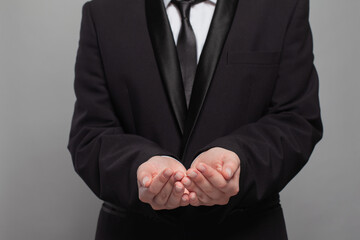 A man in a black suit is holding his hands out in a gesture of surrender