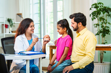 Indian Female dentist explaining dental hygiene to little girl sitting on father’s lap in clinic