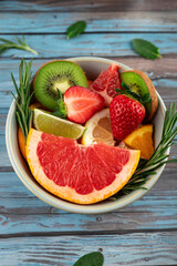 Top view of colorful mix of fresh fruits, grapefruit, strawberries, kiwi, lime and orange in a bowl decorated with rosemary and mint leaves. Natural ingredients and vibrant textures. 
