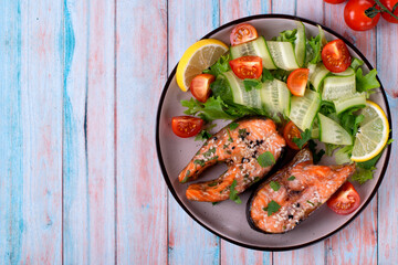 Baked trout steaks served with fresh cucumber, tomato and lettuce salad on ceramic plate. Healthy eating. Top view. Copy space