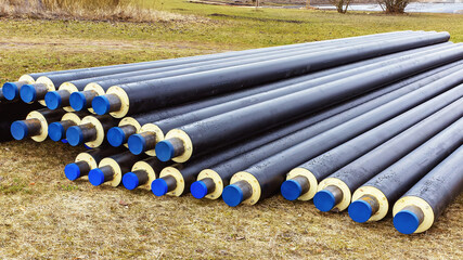 A pile of water pipes with thermal insulation in the meadow in spring