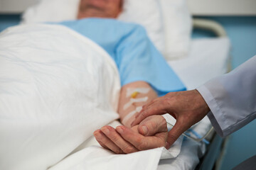 Obraz premium Doctor holding patient's hand while they lie in hospital bed equipped with medical devices suggesting supportive hospital care and compassion