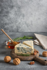 Blue cheese on wooden cutting board with honey, walnut and rosemary, grey grunge background, copy space, vertical, selective focus