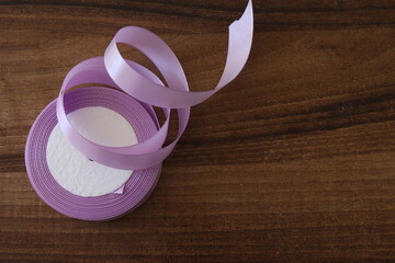 A roll of delicate lavender ribbon is gracefully unspooled on a wooden surface. The soft pastel hue contrasts with the warm, rich wood grain, creating a visually appealing and elegant composition