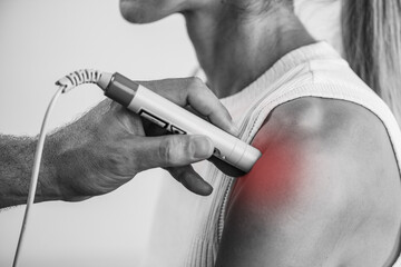 A physical therapist performs laser therapy on a patients shoulder to reduce pain, decrease...