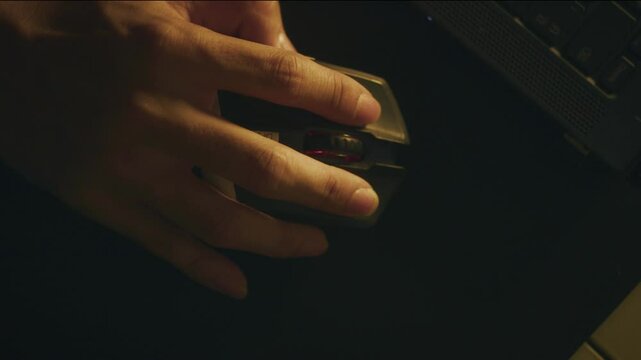 Close up of hand holding computer mouse working late night dim lighting, technology concept with dark background, softly illuminated close up creating focused atmosphere for late night productivity.