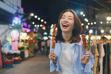 Happy young Asian woman walking in the night market,woman enjoying street food at local night market