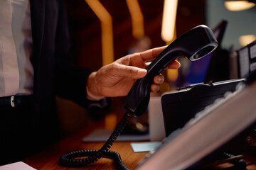 Close up of hotel manager talking on the phone at reception desk.
