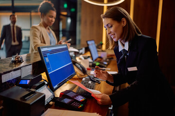 Happy receptionist going through paperwork during guest registration at hotel.