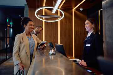 Happy black businesswoman checking in at hotel reception desk.