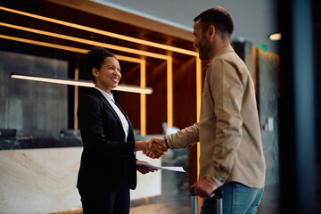 Happy black hotel manager greeting guest in hallway. © Drazen
