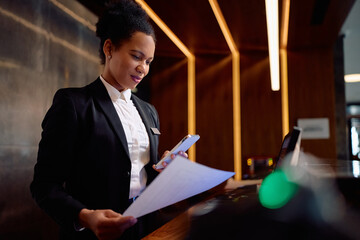 Smiling black hotel manager working at reception desk.