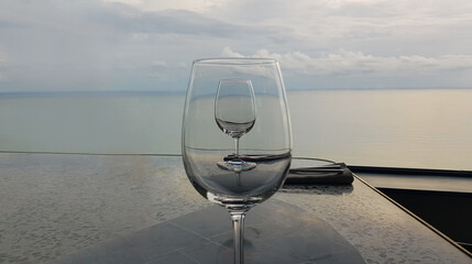 Empty wine glass on restaurant table against a sea and sky. Сalm and romantic resort background