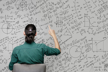 A woman is sitting near a wall with a drawing of mathematical equations, graphs amd diagrams and pointing on it. Idea generating and thinking concept