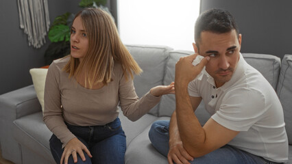 Obraz premium Woman and man having a serious conversation on a sofa in a cozy living room with a decorative plant and modern decor, suggesting home intimacy and relationship discussion.