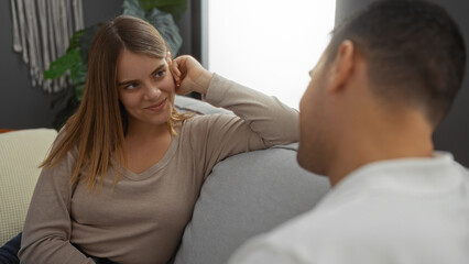 Woman and man sitting together in a cozy living room, smiling and talking, showcasing a warm relationship in an intimate home setting, creating a loving, beautiful atmosphere.