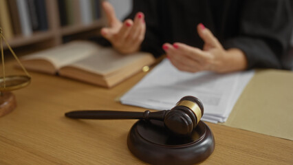 Woman talking in a courtroom with gavel on desk, hands gesturing near open book suggesting legal...