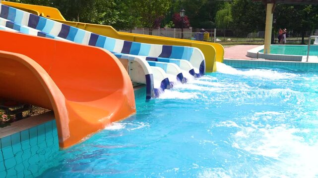 Two people arriving at the end of colorful toboggans in a waterpark during the day, medium shot, handheld