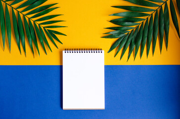 A blank spiral notebook on a yellow background with green palm leaves. Creating a tropical and minimalist design.