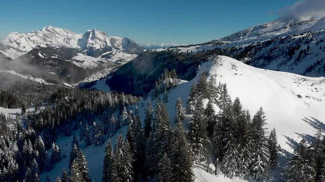 Aerial flyover over mountain peak with hikers overlooking Swiss Appenzell Alps and Santis with trees in fresh snow powder on a sunlit winter day