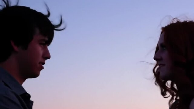 Whispers of the heart: Two young people with hair blowing in wind, bathed in the warm hues of sunset, gaze intently at each other. Capturing the raw emotion.