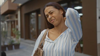 Young woman outdoors in urban city street with a pained expression, possibly due to neck...