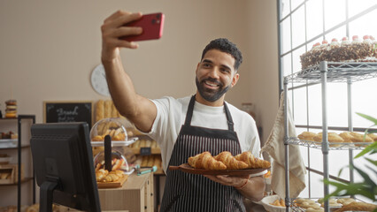 Young man taking selfie at bakery holding croissants, smiling in trendy urban shop, incorporating...
