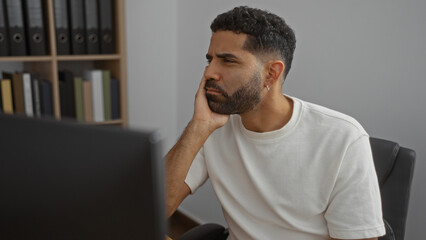 Young man working at an office desk, appearing focused and pensive, in a professional indoor...