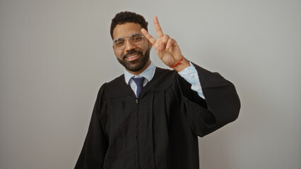 Young man in graduation gown smiling and making peace sign on isolated white background