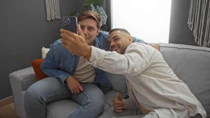 Obraz premium Two happy men sitting on a couch in a cozy living room taking a selfie with a smartphone in a modern apartment interior