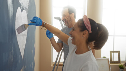 Hispanic couple painting a heart on a wall in their new home living room, depicting love, teamwork, and happiness.