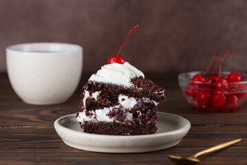 Piece of brownie cake, Black forest or Schwarzwald dessert with chocolate biscuit , whipped cream and cherries on a wooden table. Vegan dessert.