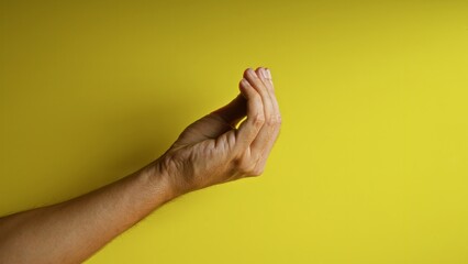 Man's hand making an italian gesture against a vibrant yellow background in a close-up shot...