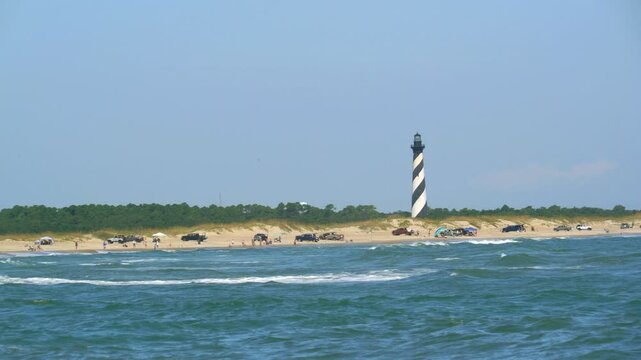 Cape Hatteras lighthouse of North Carolina with the ocean and beach lined with parked trucks and tourists.