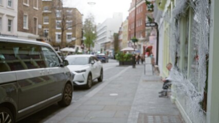 Naklejka premium Blurry street scene in london featuring defocused cars, people, and buildings capturing the essence of a winter day in the uk with a man seated on the sidewalk.