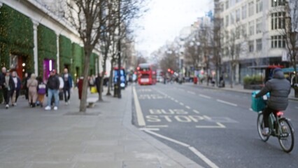 Obraz premium Blurred pedestrians walking along a busy london street with iconic red buses on a cool winter afternoon in england, featuring defocused urban scenery and cycling activity.