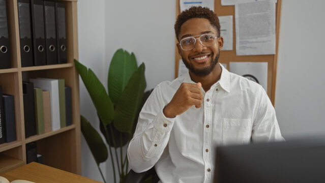 Handsome man smiling confidently in an office environment with plants and shelves in the background